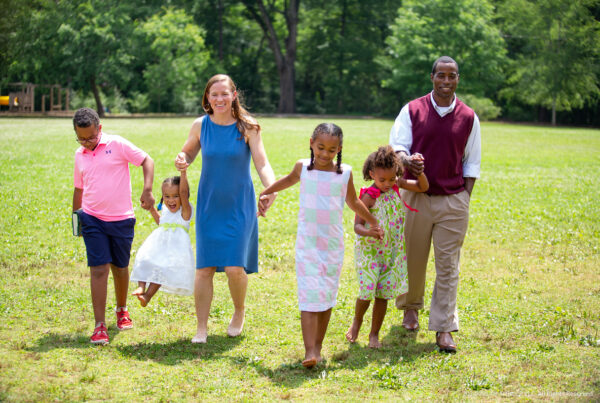 happy mixed race family (parents and four kids) walk across grassy field