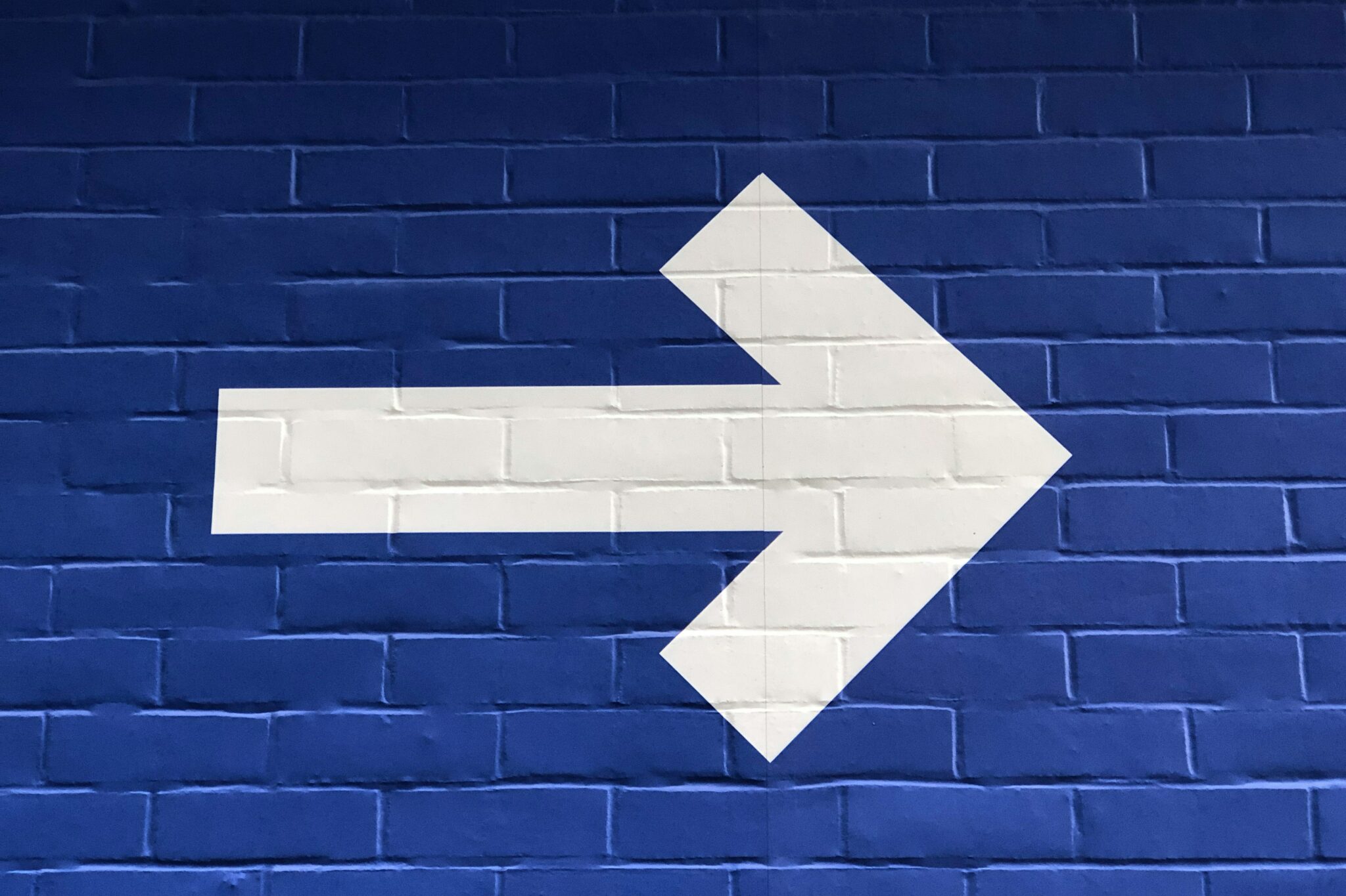 flecha blanca pintada en pared de ladrillo azul